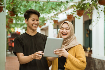 students male and hijab girl happy when looking to the screen of the tablet while chatting about with achievement