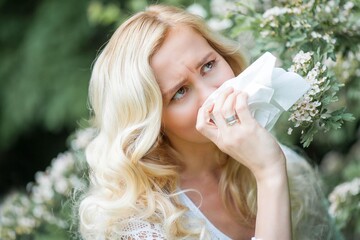 Portrait of a beautiful young blonde suffering from allergies. Spring portrait of a young woman near white blossoms.