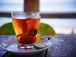 Glass of steaming black tea on saucer, with a slice of lime. Front view