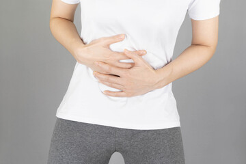 A human having painful stomachache on gray background.Chronic gastritis. Abdomen bloating concept.Close-up Of Woman using hands touching belly position suffering during menstruation period