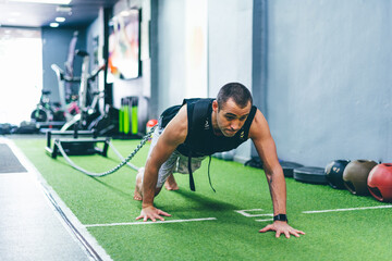 Latin boy doing physical exercise in gym dragging a sled with weight.