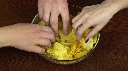 Hands of people take chips from a large plate. The company of friends eats potato chips. Hands close up
