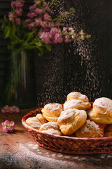Obraz na płótnie Canvas Homemade profiteroles with vanilla cream in a basket, rustic wooden table, sunny light in the kitchen, dark background with flowers, Selective focus, copy space. French choux pastry balls with cheese.