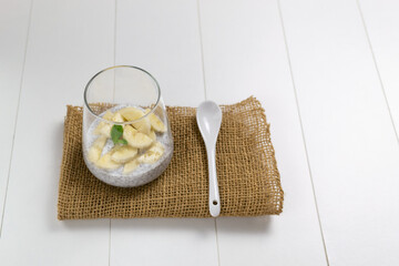 Chia pudding with banana in a glass machine with a spoon on a white background. Copy space. A...