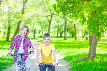 Fototapeta na wymiar Sporty family leisure. Mother and son standing with bicycles in sunny summer park. Empty space for text