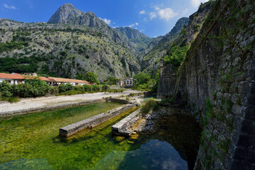 Beautiful landscape of Montenegro: red tiled roofs, river, mountains, green vegetation and blue sky with clouds.