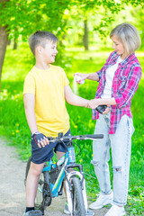 Obraz premium Caring mother spraying insect repellent or sunscreen lotion on skin her young son, while he ride a bike at summer sunny park