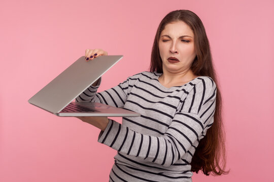 Portrait Of Displeased Girl In Striped Sweatshirt Closing Laptop, Looking With Suspicious And Distrust At Screen, Scared Of Unknown Software, Failure, Program Bug. Indoor Shot, Pink Background