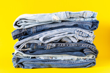 A stack of different jeans trousers close up on a yellow background, casual clothes