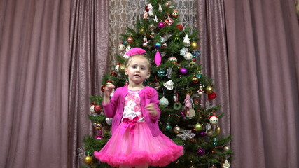 Little girl is spinning on the background of the Christmas tree. Christmas tree decorated with Christmas toys and lights.