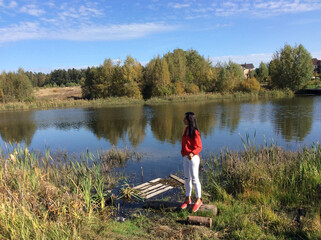 A young woman brunette resting stands near the forest, on the shore of the lake. Sunny and warm day.