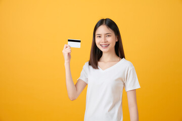 Attractive smiling Asian woman holding credit card payment on yellow background with copy space.