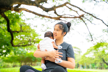 Naklejka premium Mother hold carry infant baby boy sitting under tree branch