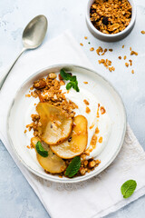Greek yogurt with caramelized pear, granola, nuts and melted sugar for a wholesome breakfast on a gray ceramic plate. Rustic style. Top view.