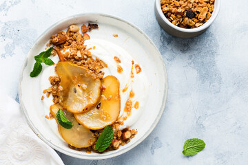Greek yogurt with caramelized pear, granola, nuts and melted sugar for a wholesome breakfast on a gray ceramic plate. Rustic style. Top view.