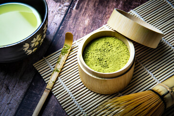 Green Tea Matcha Powder in the Bamboo Cup with Wooden Chasen in Matcha Tea Bowl and Wooden Spoon and on Wooden Background