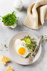 Traditional English breakfast with fried eggs with arugula microgreen in gray ceramic plate on gray concrete old background. Top view.