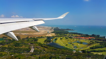 Airplane wing in blue sky over the city over the golf course. Sea with ships in the background....