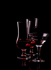 Glass wine glasses of different sizes. Beautiful glasses on a black background with a cherry.