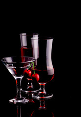 Glass wine glasses of different sizes. Beautiful glasses on a black background with a cherry.