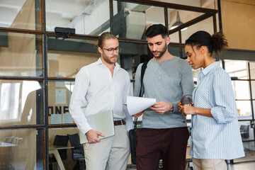 Photo of multinational focused colleagues talking and reading documents