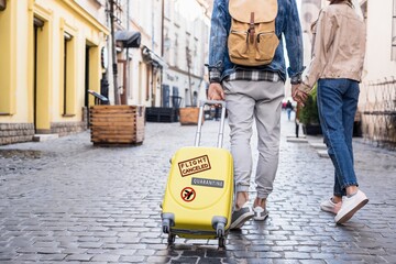 Cropped view of couple walking with travel bag on street, quarantine illustration