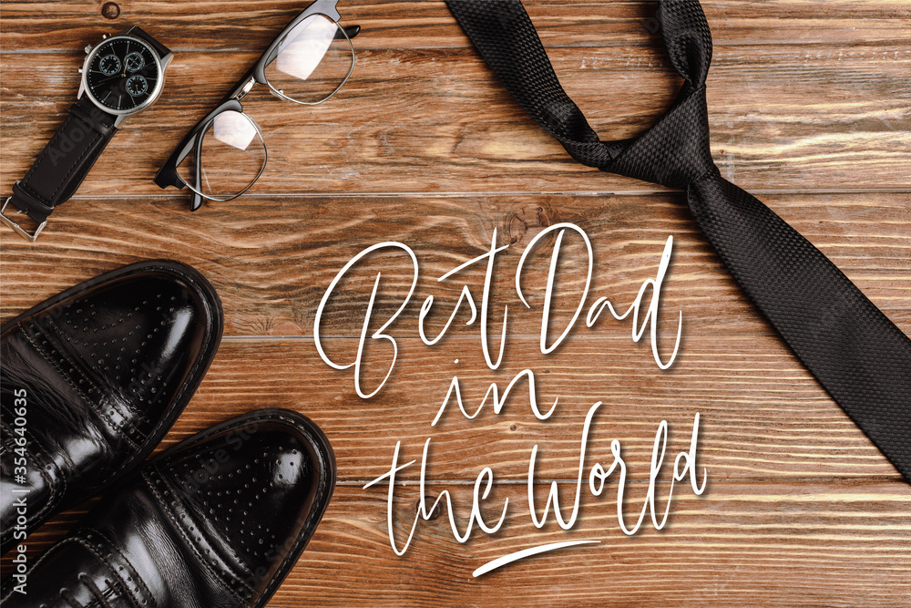 Wall mural top view of mens black shoes, tie, wristwatch and glasses on wooden background, best dad in the worl