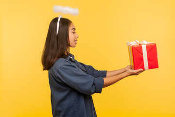 Take this holiday present! Side view of kind generous angelic girl with holy nimbus giving birthday...