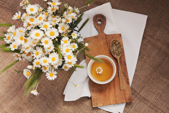 Cup of chamomile tea, bouquet of chamomile flowers, dried flowers in wooden spoon on cutting board. Doctor treatment, immune concept, traditional medicine