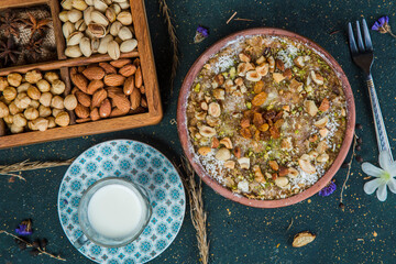 Umm Ali on table with nuts and milk. Oriental dessert with Egyptian bread and chopped nuts on table next to cup of milk and box with almonds, star anise, hazelnuts and pistachio.