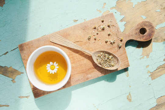 Cup of chamomile tea with chamomile flower, dried flowers in wooden spoon on cutting board. Doctor treatment, immune concept, traditional medicine