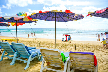 People going to beach under bright sunny sky with benches and colorful beach umbrella by the sea, Phuket, Thailand. Summer beach activity background