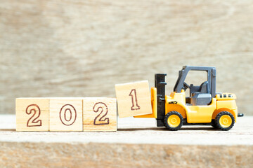 Toy forklift hold letter block 1 to complete word 2021 on wood background