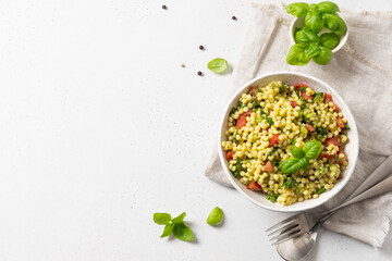 Vegetable salad with pasta ptitim or Birdy, Israeli couscous decorated basil leaves on white . Top view.