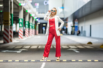 young blonde schoolgirl in a red suit and a white jacket posing in the parking lot