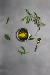 Small metallic bowl and spoon full of olive oil, and cuttings from olive tree with leaves and...