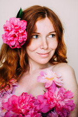 Obraz na płótnie Canvas Redhead girl with freckles dressed in pink peonies flowers as in a dress with naked shoulders. Natural beauty. The concept of self-love and appearance.