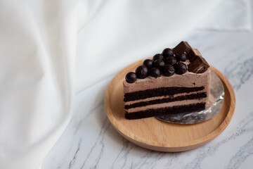 Slice of chocolate cake with chocolate ball on white marble background.