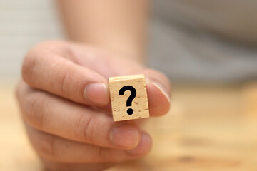 A man hold and shows wooden block with question mark on it, concept of asking question or doubt
