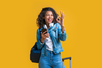 Happy cute casually dressed tourist girl with backpack and mobile phone winking and showing ok...