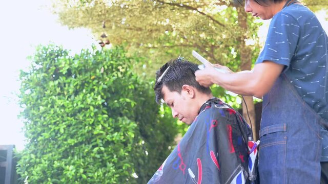 Asian making haircut at home garden. Learning online barber courses during lockdown for new occupation. New normal life after Covid-19 outbreak pandemic situation.