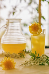 Citrus lemonade in a glass and a jug stands on a table among fresh flowers