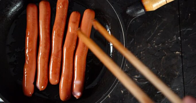 Male hand turns the sausages in the pan.