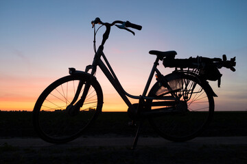 Naklejka premium Bicycle is silhouetted against a colorful evening sky after sunset