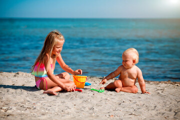 Children play on the beach. Summer water fun for the family. Boy and girl with toy buckets and a shovel on the seashore.