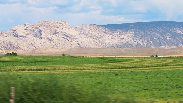 Jensen, Utah driving pov point of view of agricultural green field and Dinosaur National Monument in slow motion with desert canyons in summer and window perspective of mountains