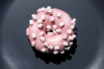 Top view of delicious single pink donat with white marshmallows on the dark grey ceramic plate. Creartive sweet food macro concept. Isolated bright tasty dessert