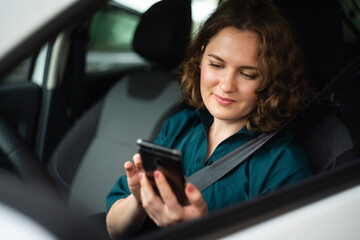 Fototapeta na wymiar Woman driver sitting in car and looking at smartphone screen