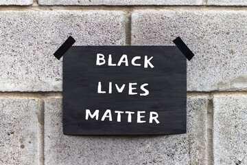 Black poster on gray brick wall. Banner with text Black Lives Matter. Anti-racism protest.