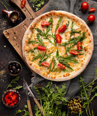 Pizza with salmon, arugula and tomato on the wooden cupboard and some ingredients and spices around 